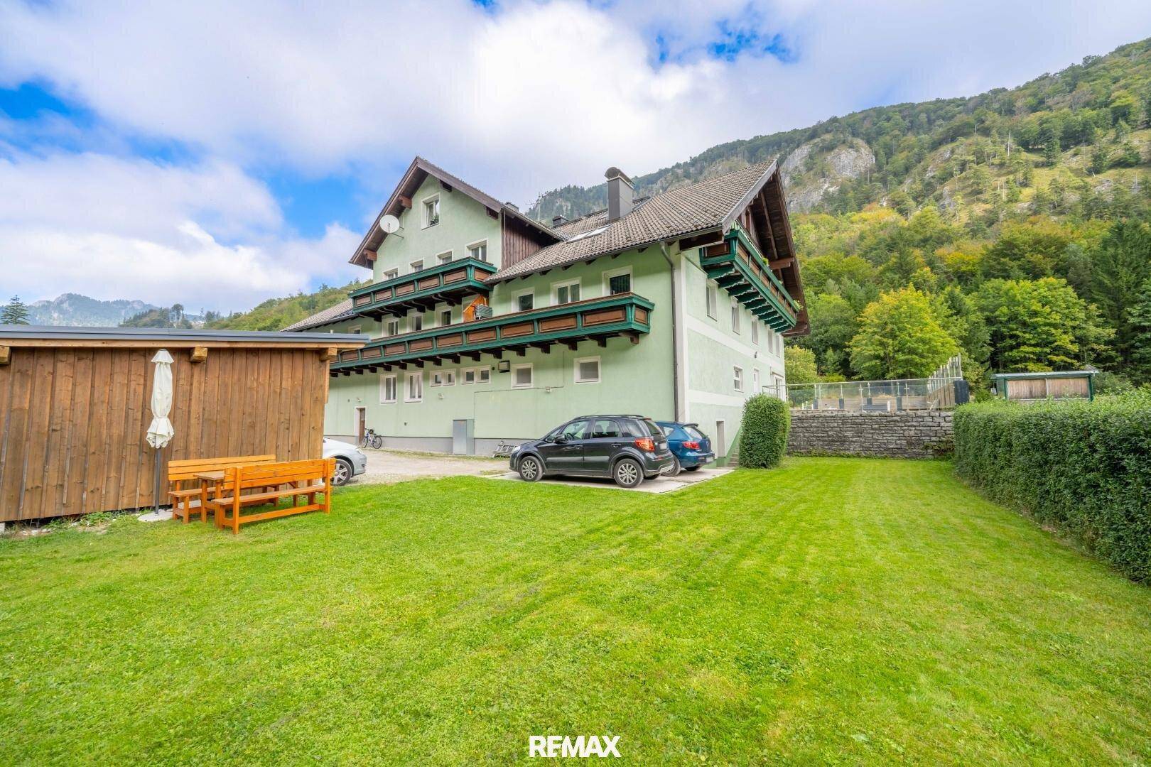 Charmantes Gebäude mit mehreren Balkonen, umgeben von grüner Natur und Bergen.