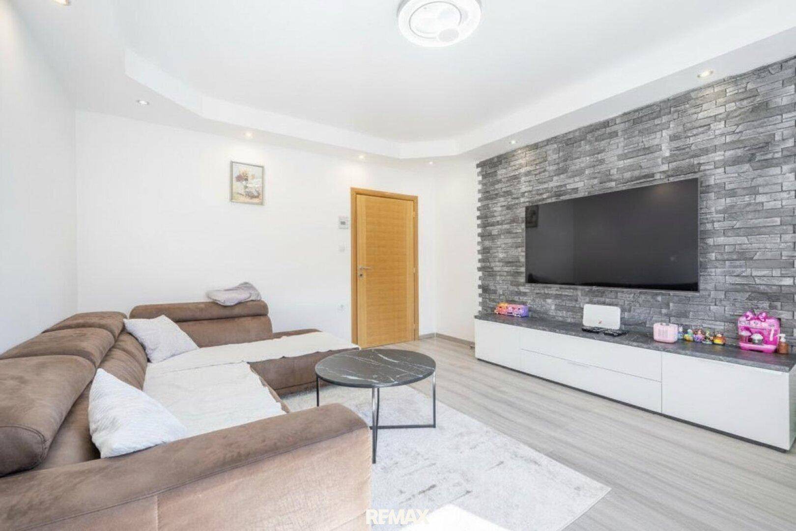 Gemütliches Wohnzimmer mit großem Ecksofa, modernem Laminatboden und einer Steinwand hinter dem Fernseher.
