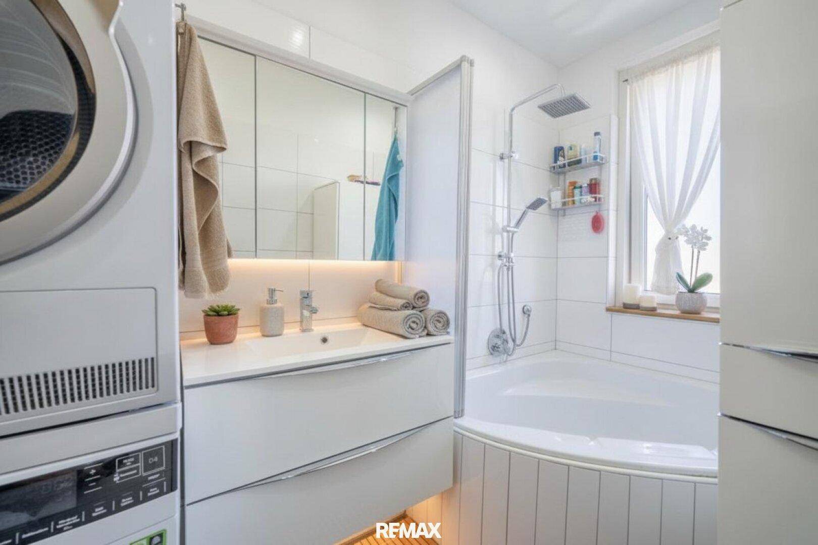 Modernes Badezimmer mit Eckbadewanne, Dusche, Waschbecken, Spiegelschrank und Waschmaschine/Trockner.