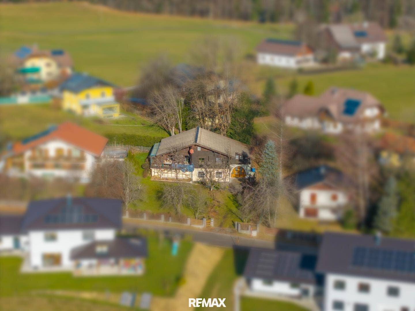 Luftaufnahme des Anwesens mit dem Holzhaus und umliegenden Häusern in ländlicher Umgebung.