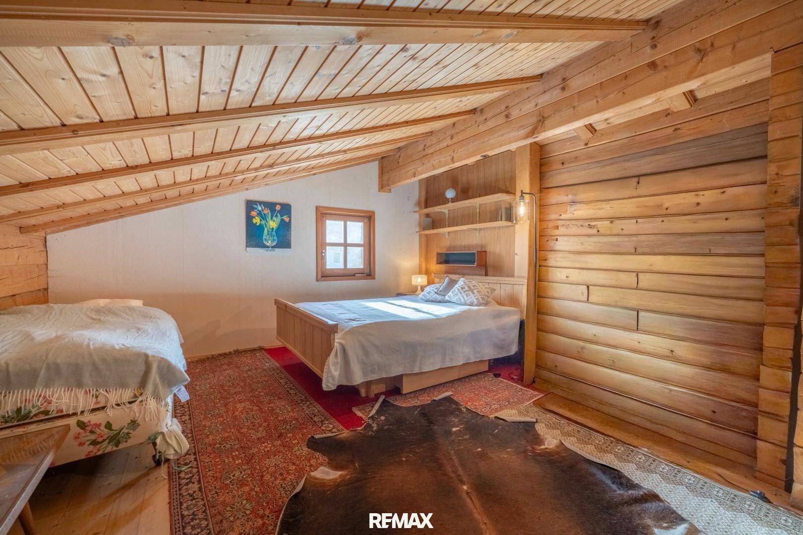 Schlafzimmer im Dachgeschoss mit schrägen Holzdecken, Holzwänden und rustikalem Teppich.