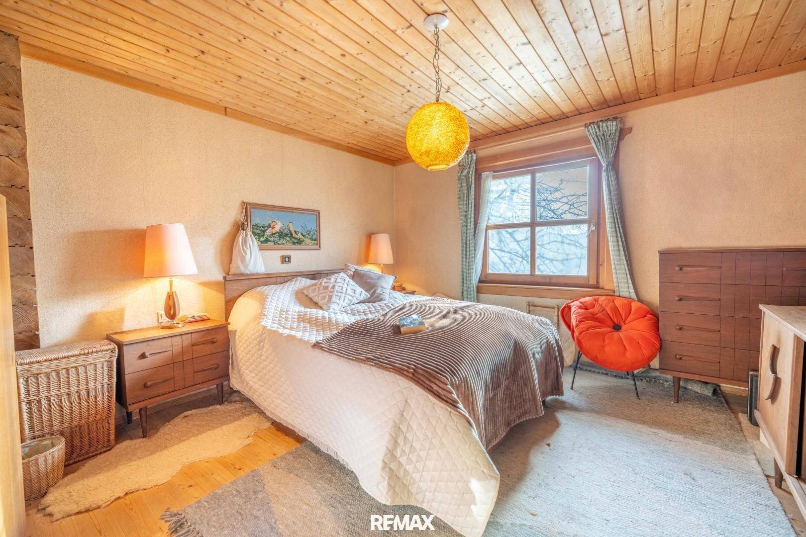 Gemütliches Schlafzimmer mit Holzwänden, Holzboden und einem Fenster mit Blick ins Grüne.
