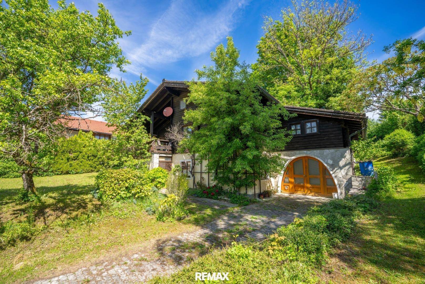 Charmantes Holzhaus mit gewölbtem Garagentor und üppiger grüner Vegetation im Sommer.