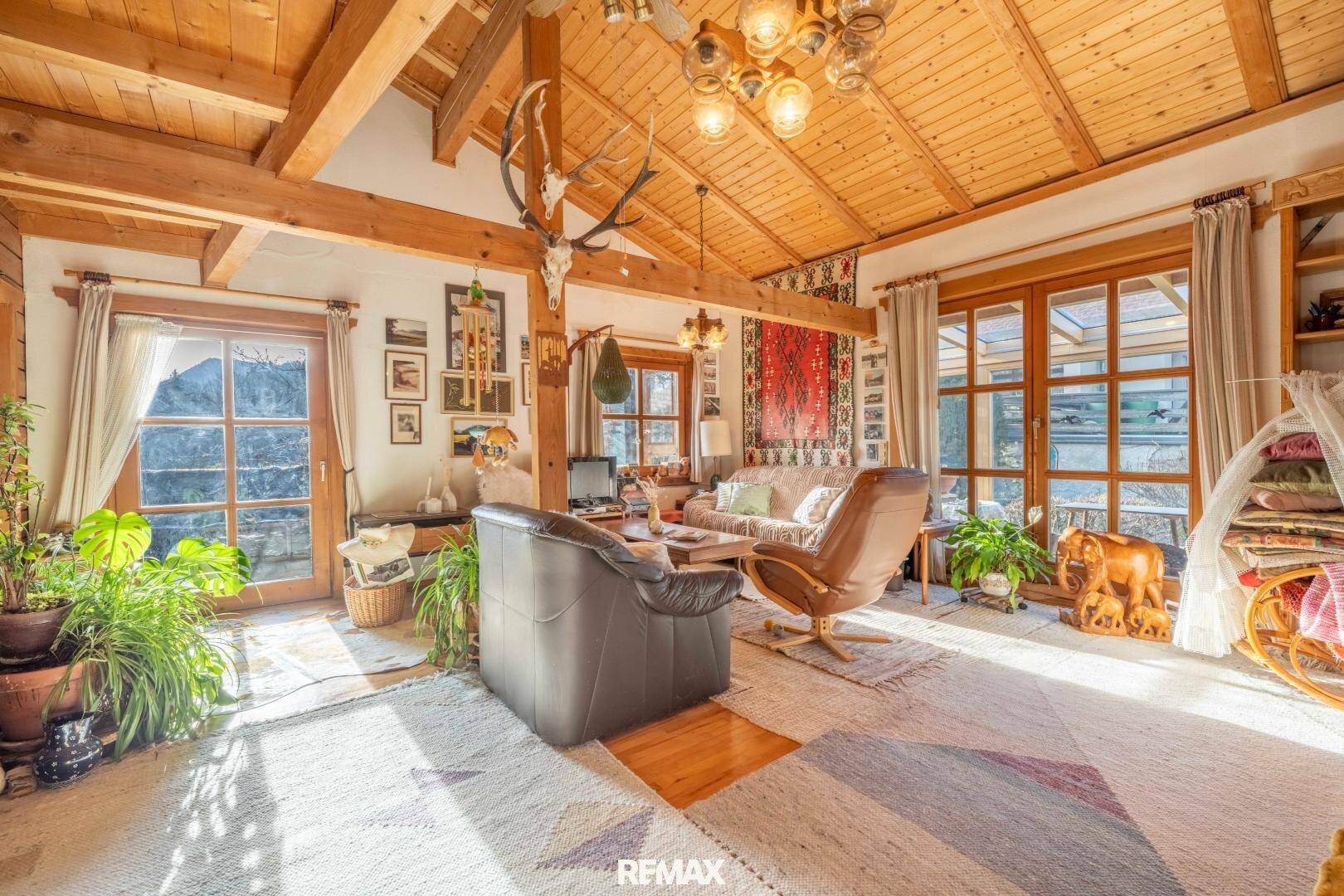 Gemütliches Wohnzimmer im alpinen Stil mit Holzbalken, großen Fenstern und traditioneller Dekoration.
