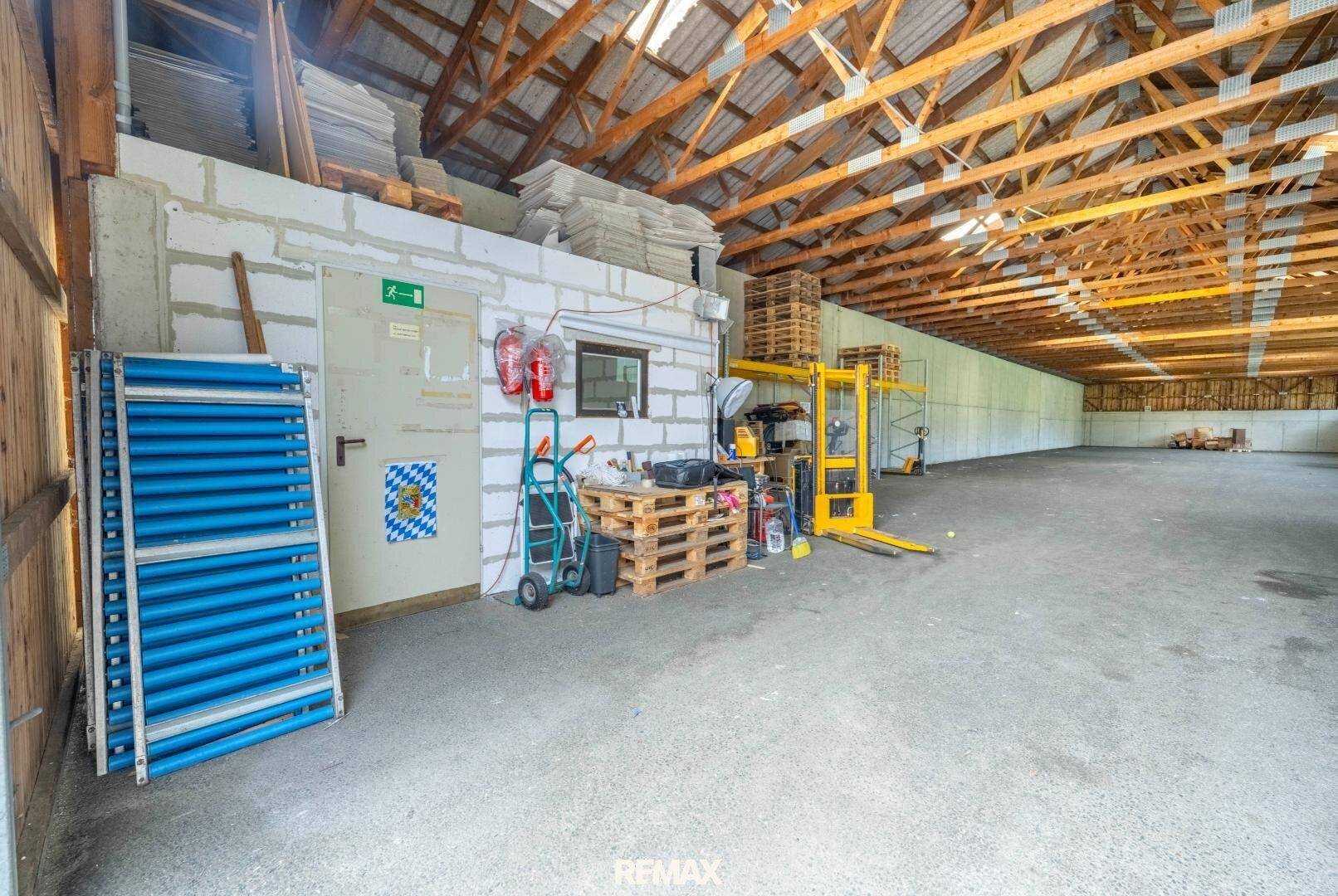 Seitenbereich einer Lagerhalle mit Zugangstür, Feuerlöschern und Lagergeräten, funktional gestaltet.