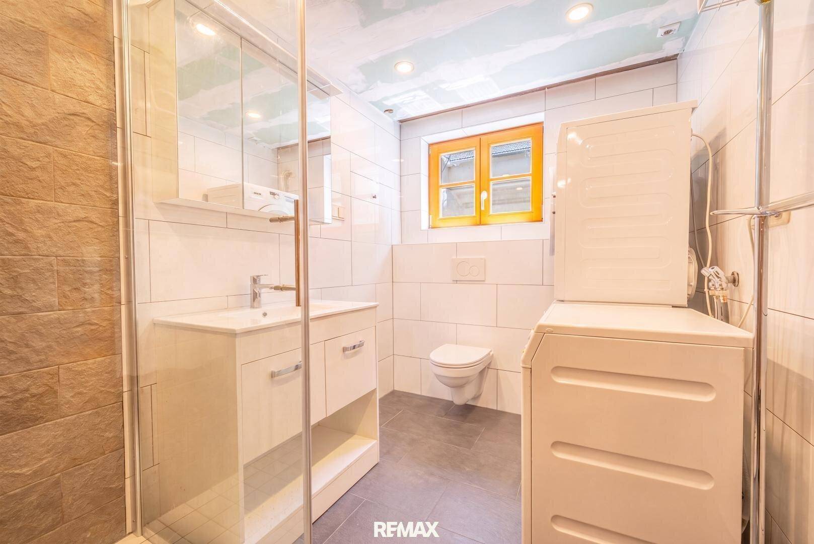 Modernes Badezimmer mit Dusche, WC und Waschmaschine.