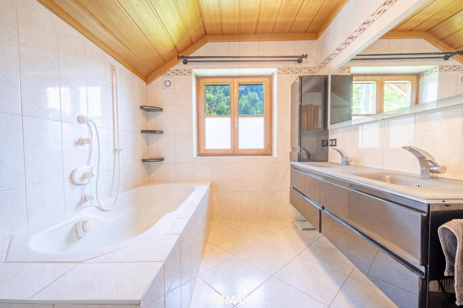 Geräumiges Badezimmer mit Badewanne, Doppelwaschbecken und Holzdecke.