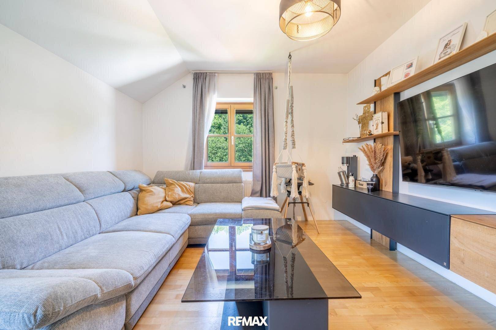 Modern eingerichtetes Wohnzimmer mit Holzboden und Blick ins Grüne durch das Fenster.