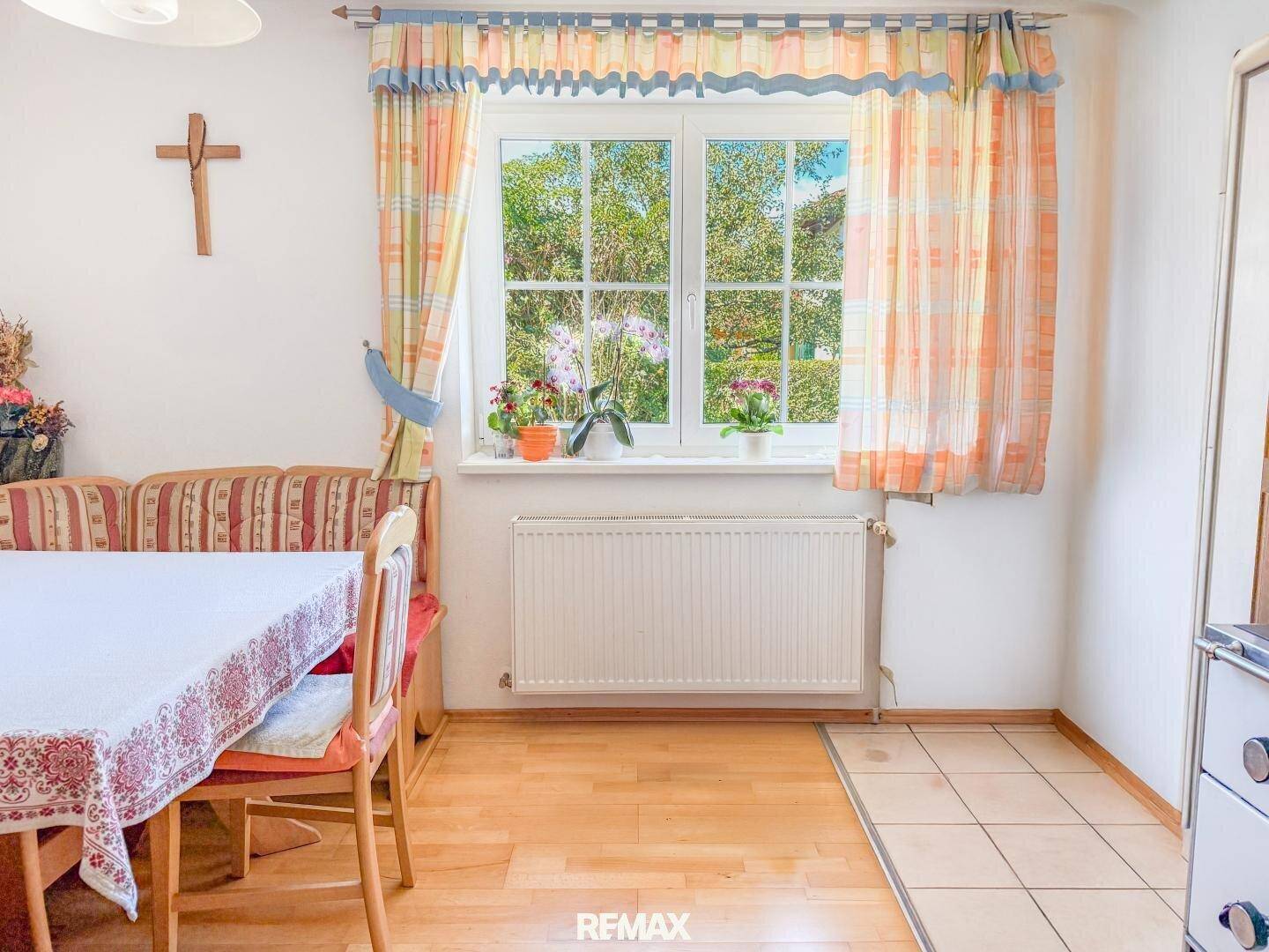 Gemütlicher Essbereich mit Holztisch, Sitzbank und Blick ins Grüne durch das Fenster.