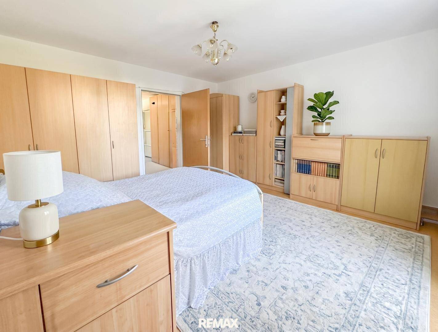 Helles Schlafzimmer mit Holzmöbeln, Teppichboden und Zugang zu einem weiteren Raum.