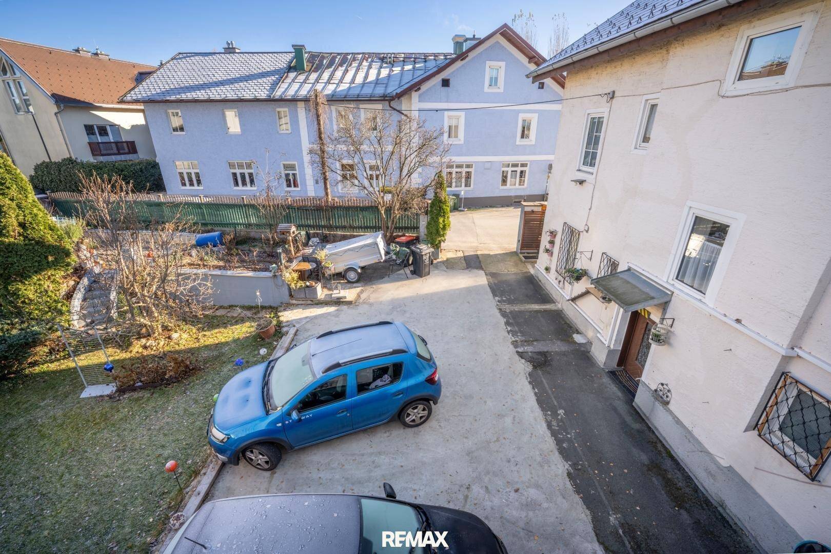 Außenbereich mit Parkplätzen und Zufahrt, umgeben von weiteren Gebäuden und Grünflächen.