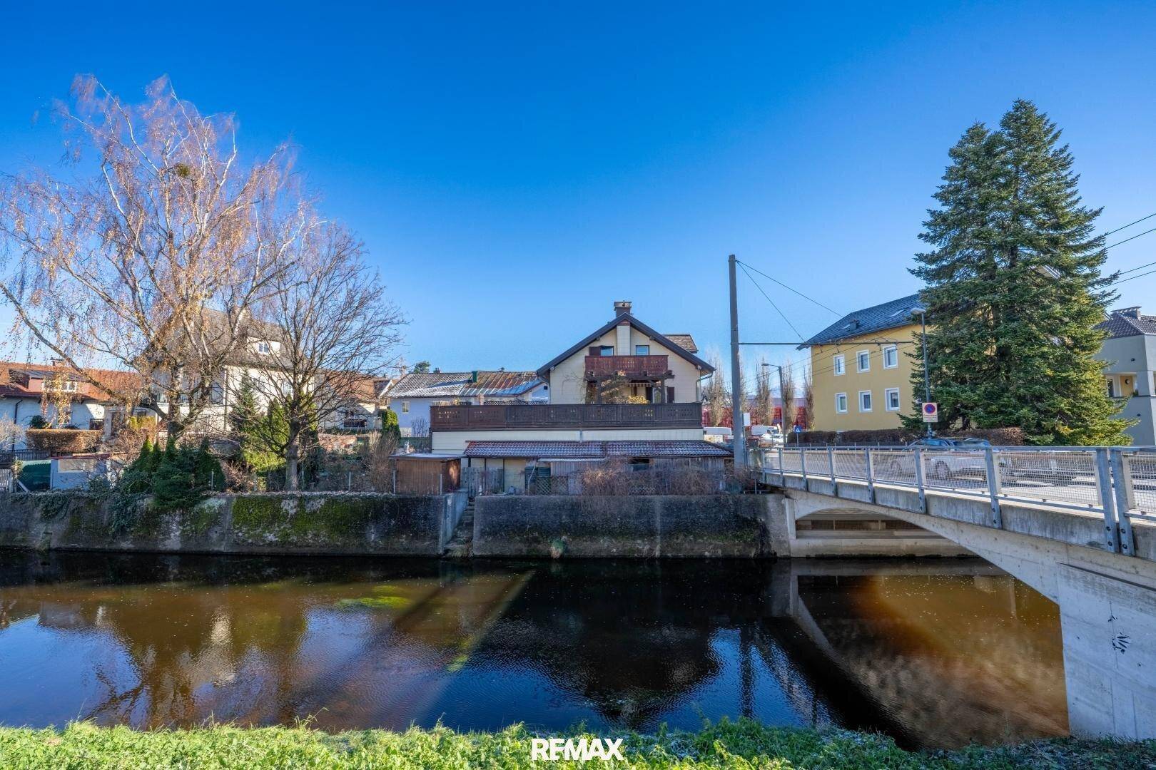 Ansicht des Gebäudes vom gegenüberliegenden Ufer eines Kanals mit einer Brücke im Vordergrund.