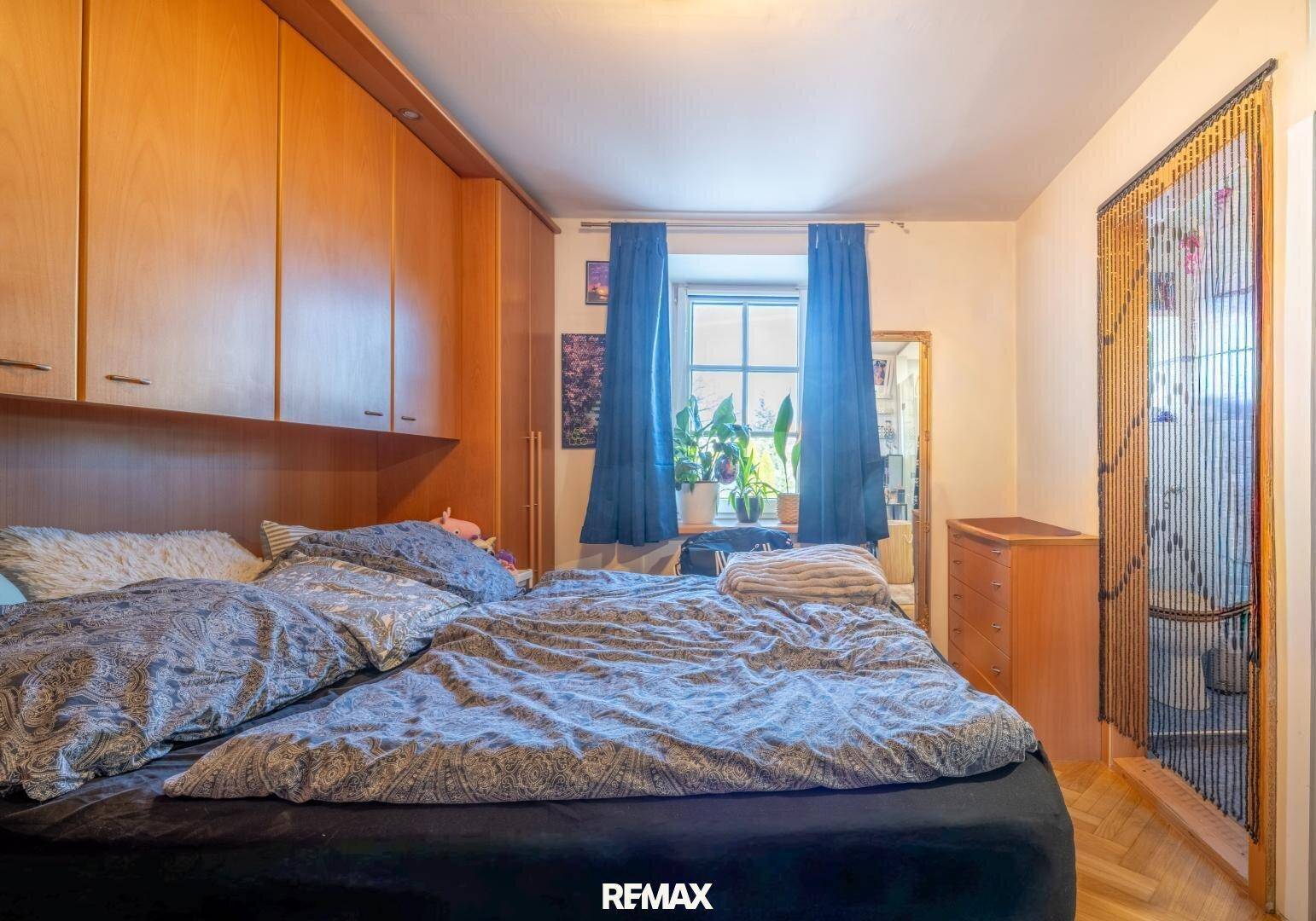 Schlafzimmer mit großem Bett, eingebauten Holzschränken und einem Fenster für natürliches Licht.