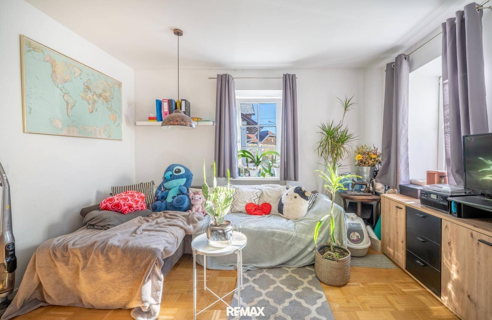 Gemütliches Wohnzimmer mit Holzboden, bequemer Couch und Fenster mit Blick nach draußen.
