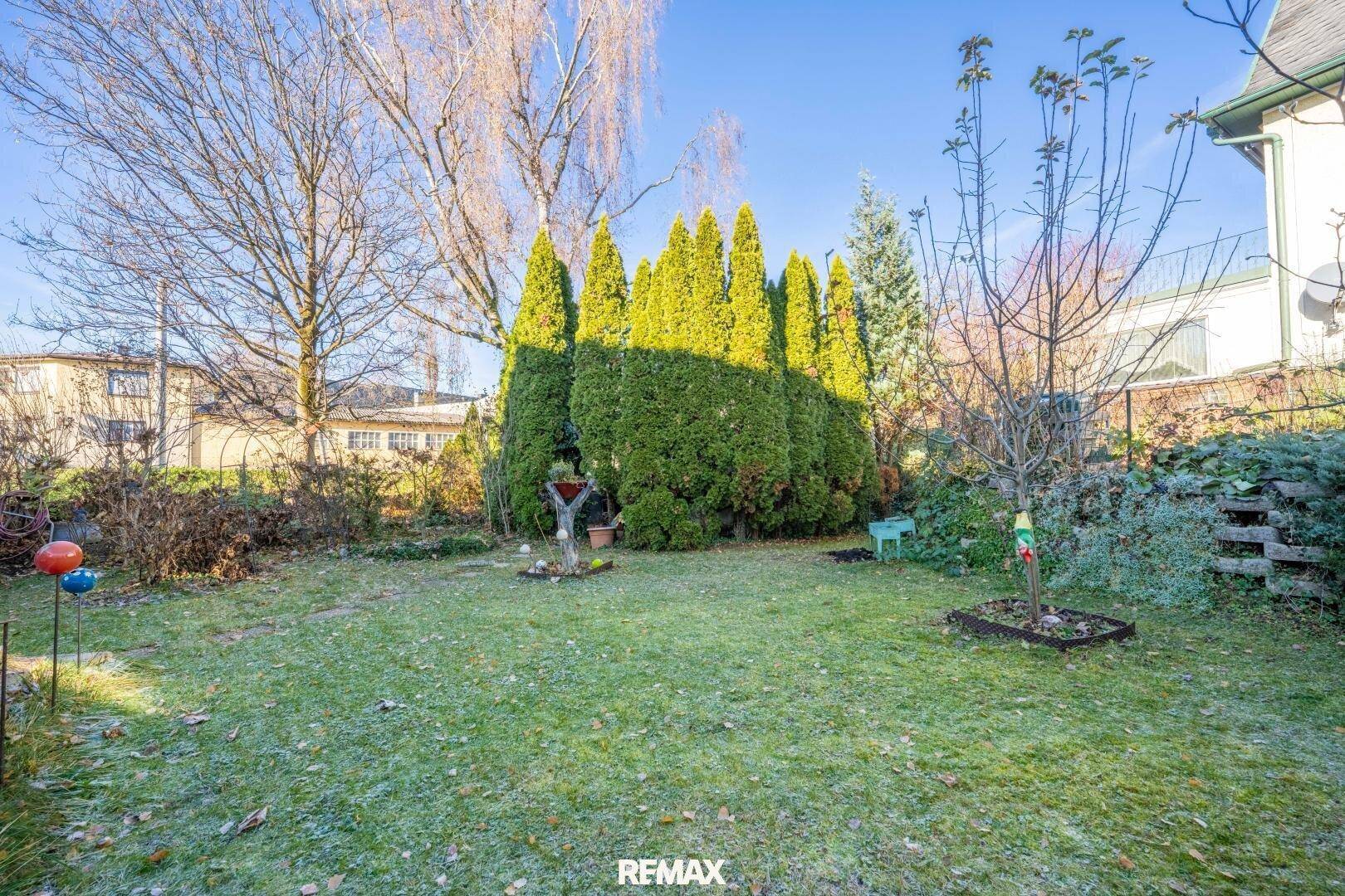 Großer Gartenbereich mit Rasen, hohen Bäumen und Hecken, ideal zum Entspannen im Freien.