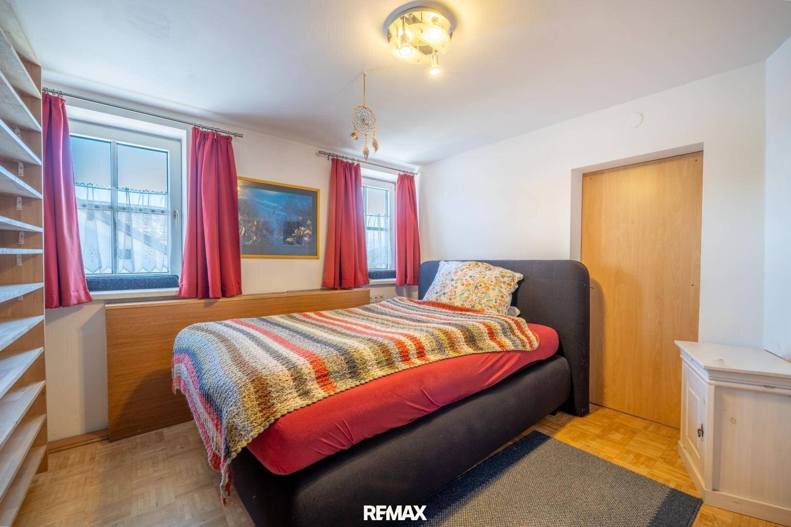 Schlafzimmer mit Einzelbett, Holzboden und zwei Fenstern, die für Helligkeit sorgen.