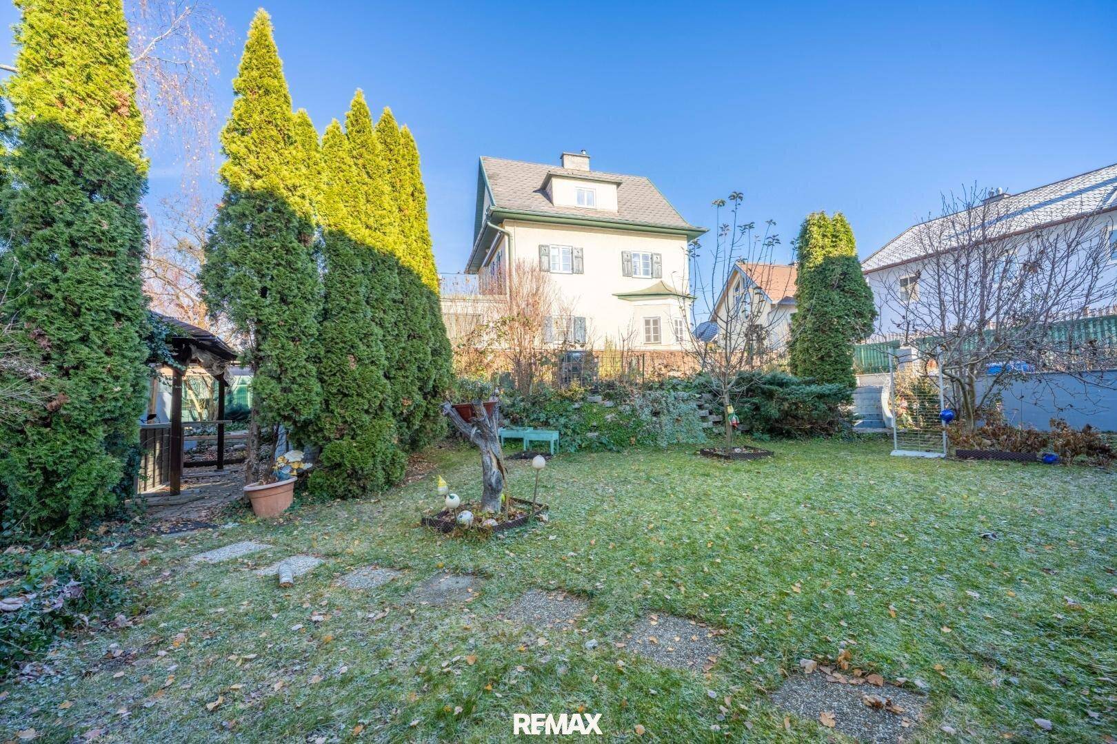 Gepflegter Gartenbereich mit Rasenfläche, hohen Hecken und einem kleinen Gartenhaus im Hintergrund.