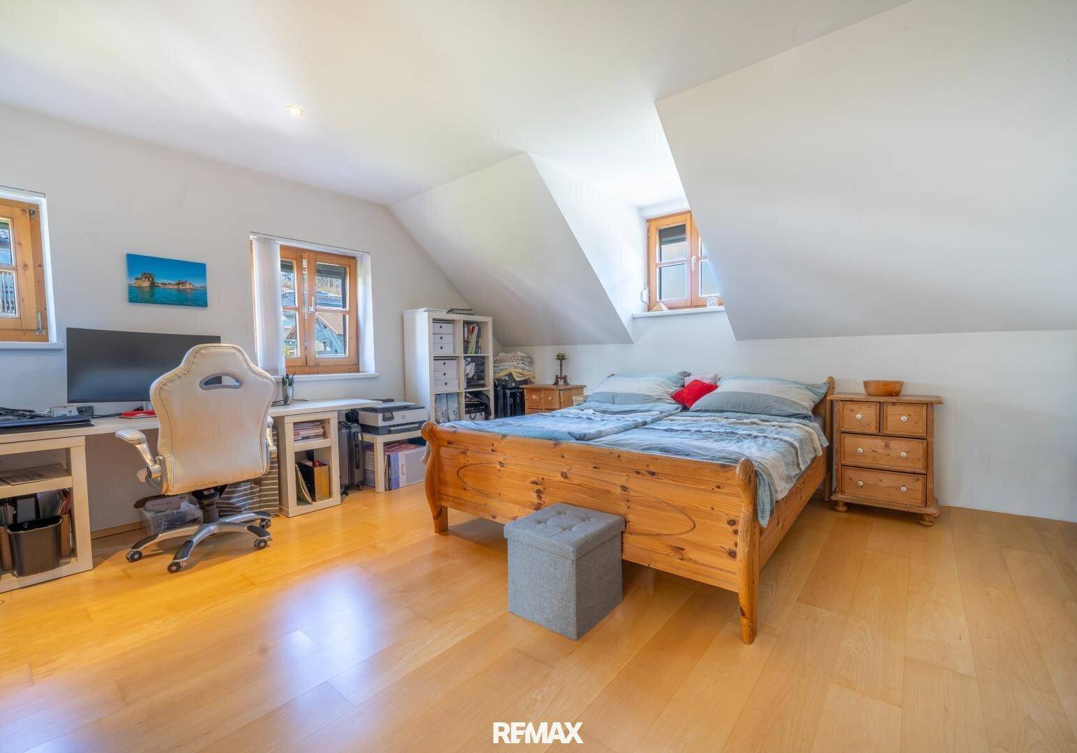 Geräumiges Schlafzimmer mit Holzdoppelbett, Schreibtisch und mehreren Fenstern unter der Dachschräge.