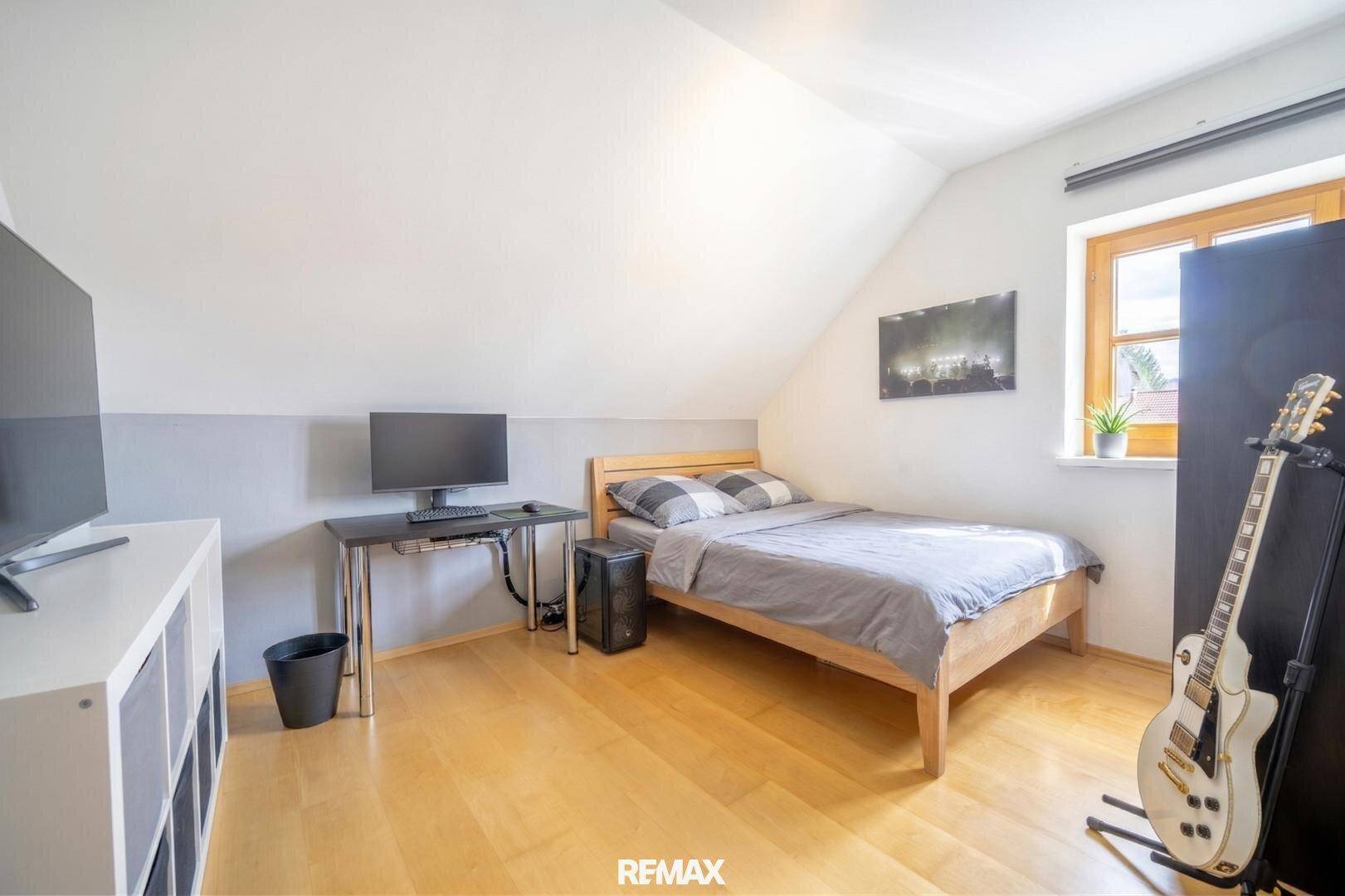 Schlafzimmer mit Einzelbett, Schreibtisch und Holzboden unter einer Dachschräge.
