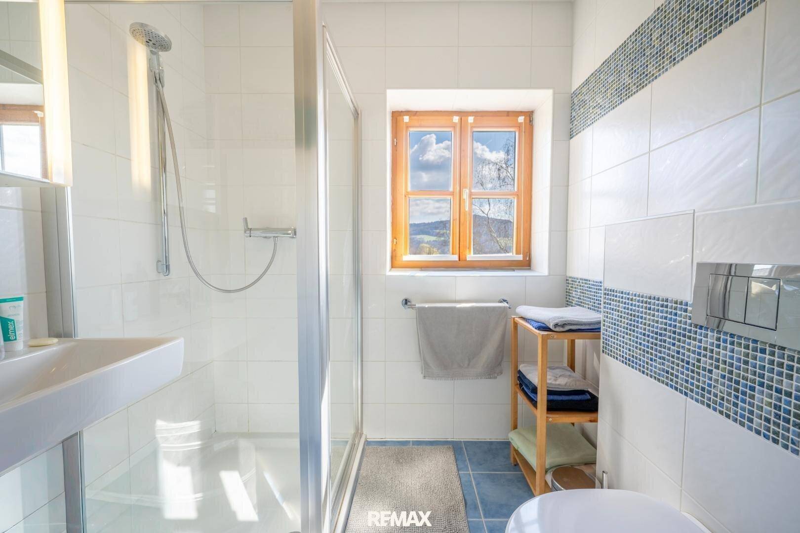 Kleineres Badezimmer mit Duschkabine, Waschbecken, Wand-WC und einem Fenster mit Bergblick.