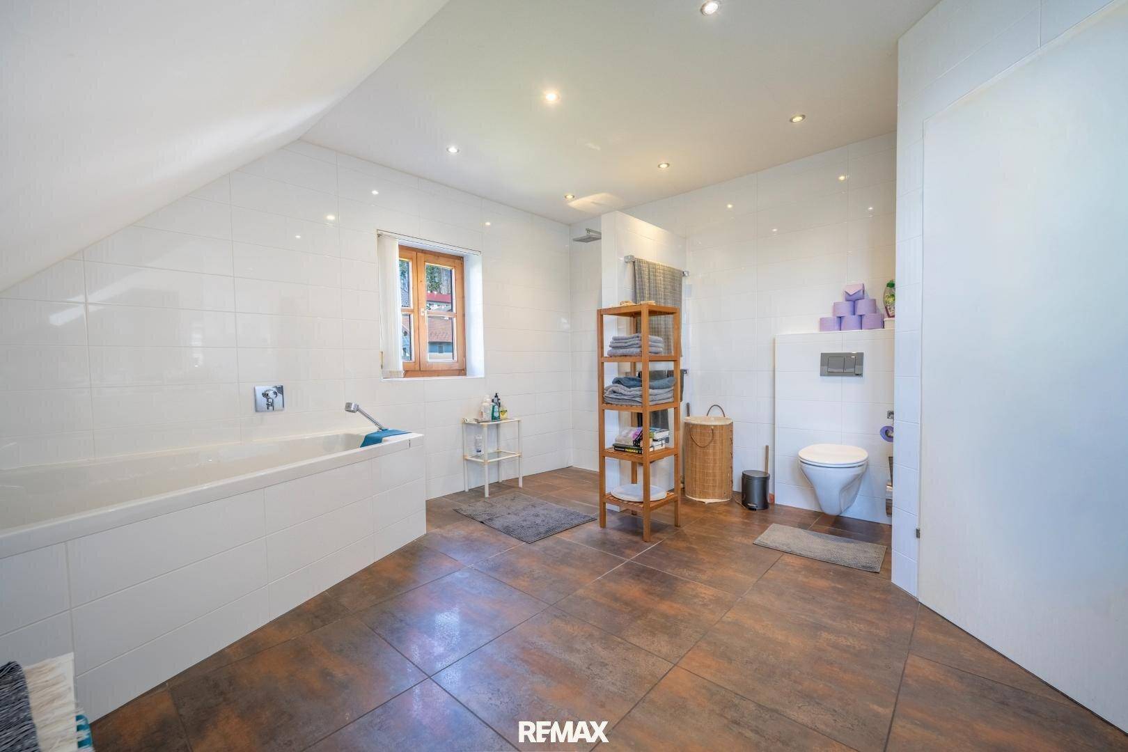 Geräumiges Badezimmer mit Badewanne, Wand-WC, Fliesen und einem Fenster unter der Dachschräge.