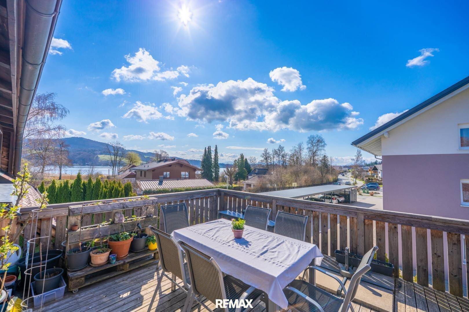 Sonniger Balkon mit Holzboden, Esstisch und weitem Blick auf den See und die Berge.