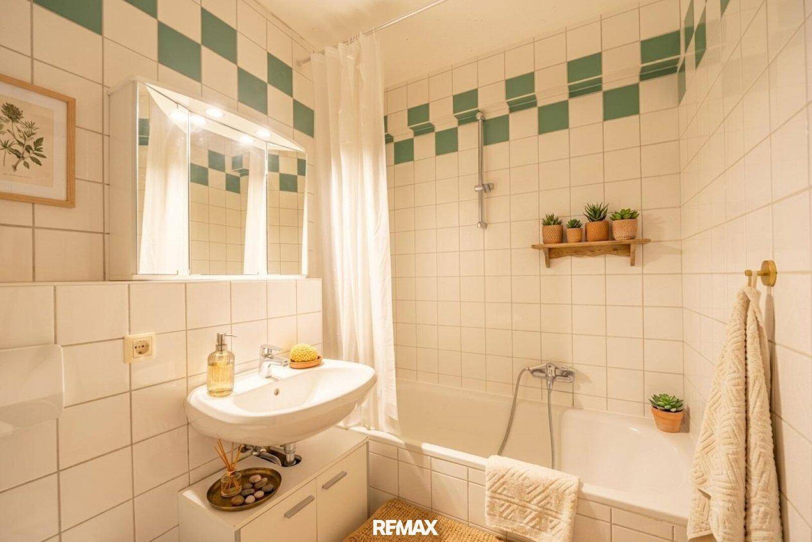 Badezimmer mit Badewanne, Waschbecken und grün-weiß karierten Fliesen.