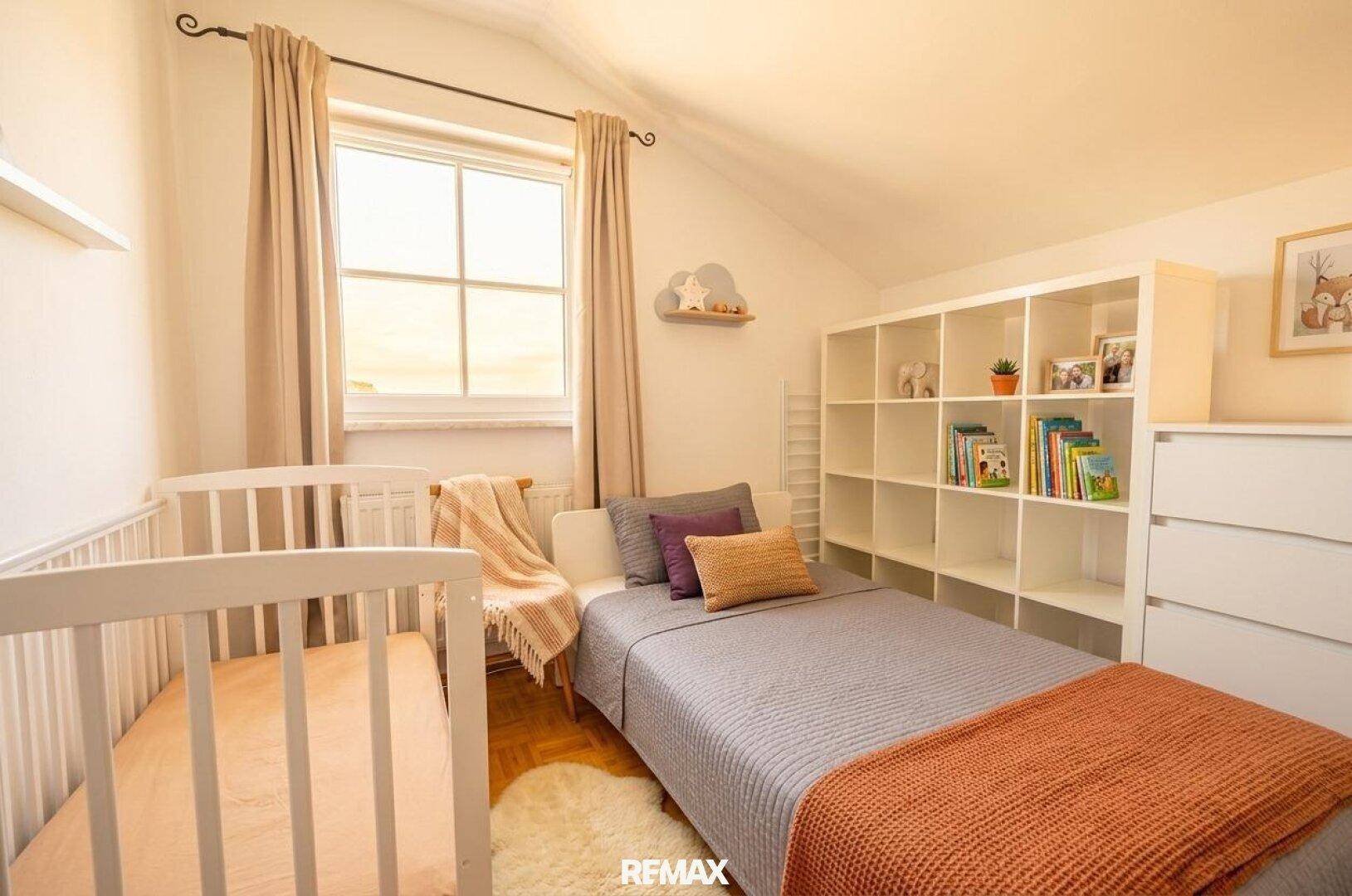 Helles Kinderzimmer mit Babybett, Einzelbett, Regal und Dachschräge.