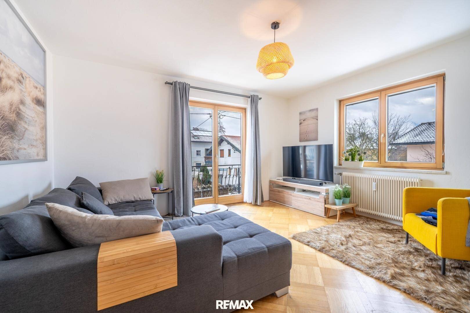 Helles Wohnzimmer mit Parkettboden, gemütlichem Sofa und Zugang zu einem kleinen Balkon.