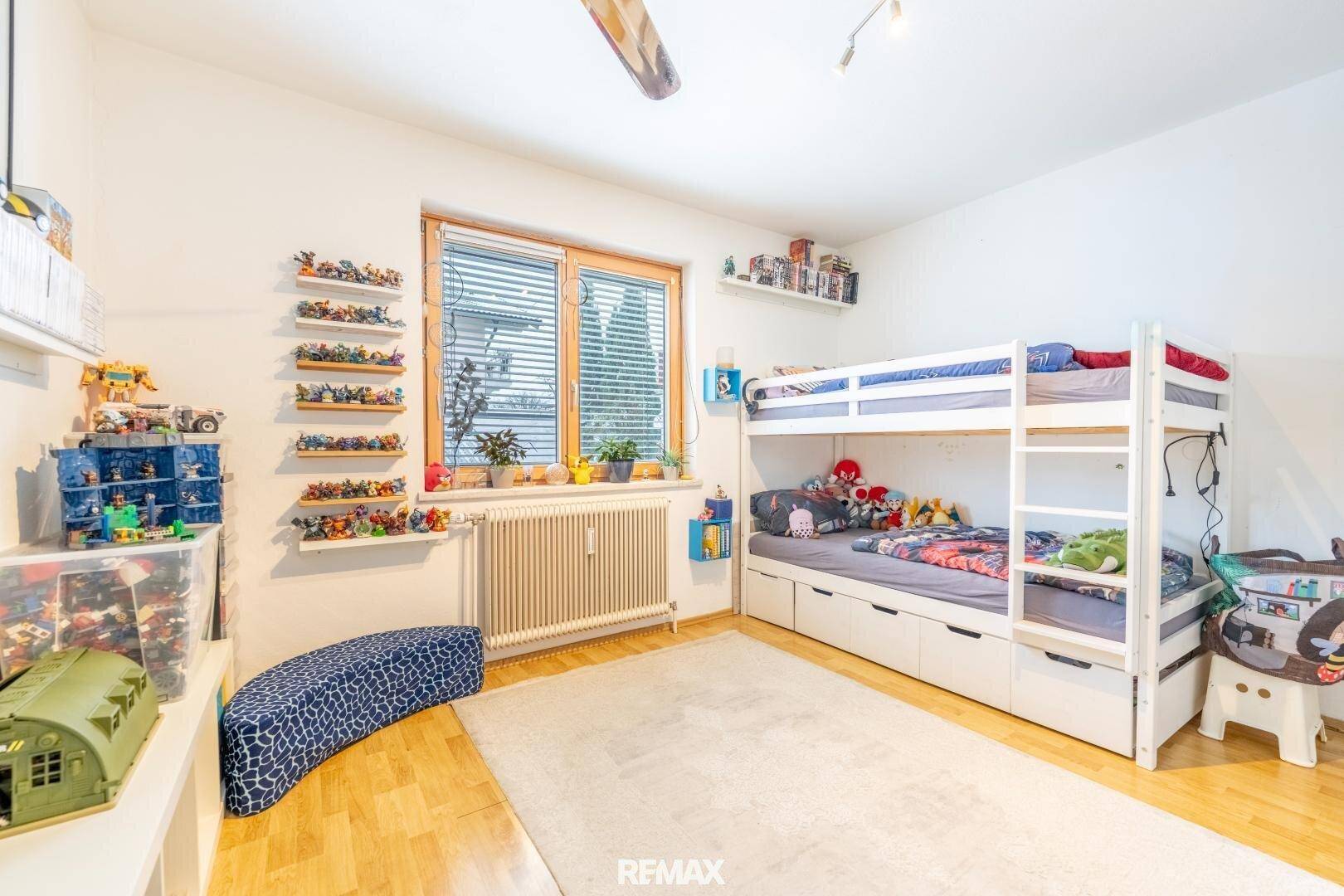 Kinderzimmer mit Etagenbett, Teppich und Fenster, hell und spielerisch eingerichtet.