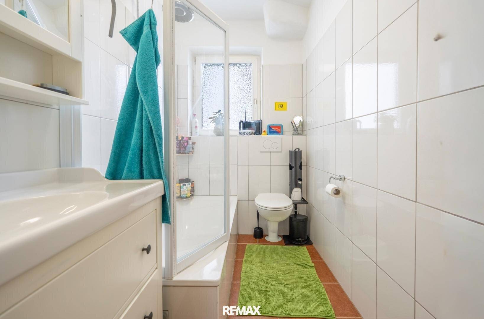 Modernes Badezimmer mit Dusche, WC und Fenster, komplett gefliest in Weiß.