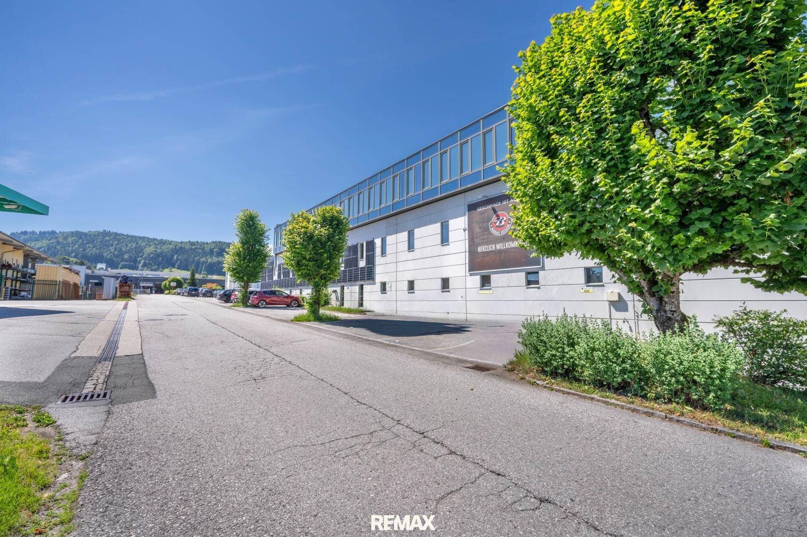 Langes, modernes Geschäftsgebäude mit vielen Fenstern entlang einer Straße, umgeben von Bäumen und Grünflächen.