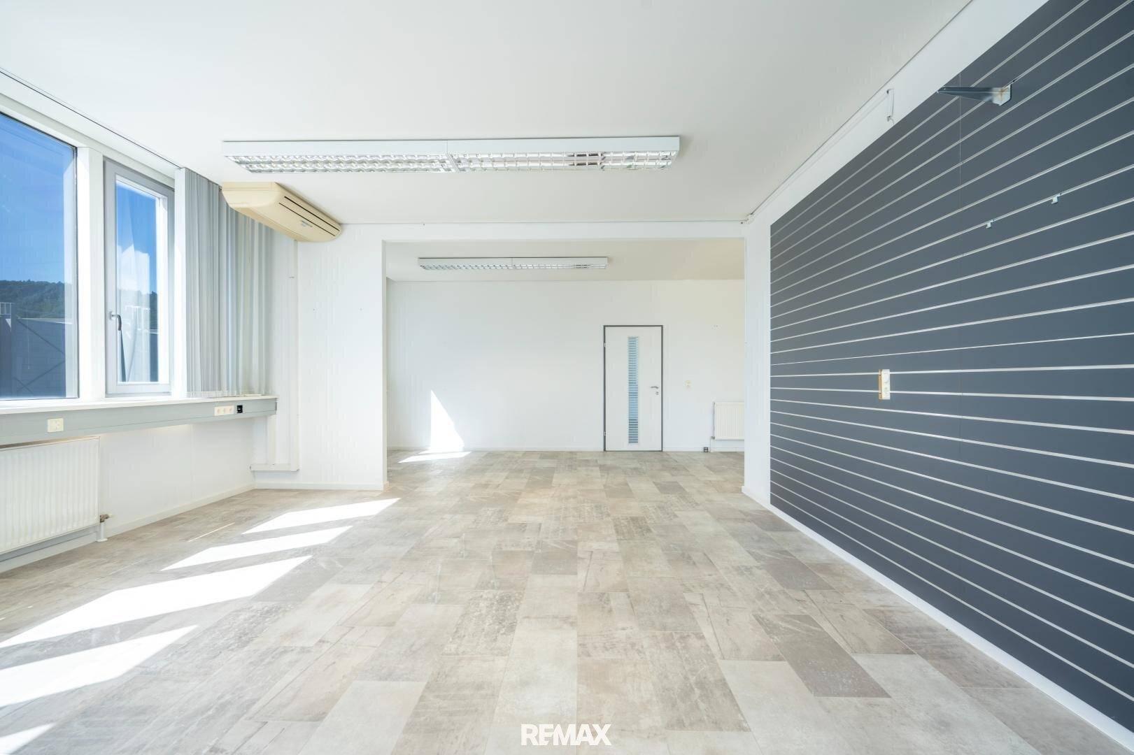 Geräumiger Büroraum mit Fliesenboden, Klimaanlage und einer dunklen Lamellenwand, ideal für flexible Nutzung.