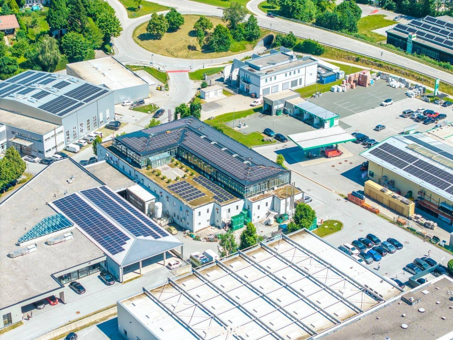 Luftaufnahme eines Gewerbekomplexes mit mehreren Gebäuden, Parkplätzen und zahlreichen Solaranlagen auf den Dächern.