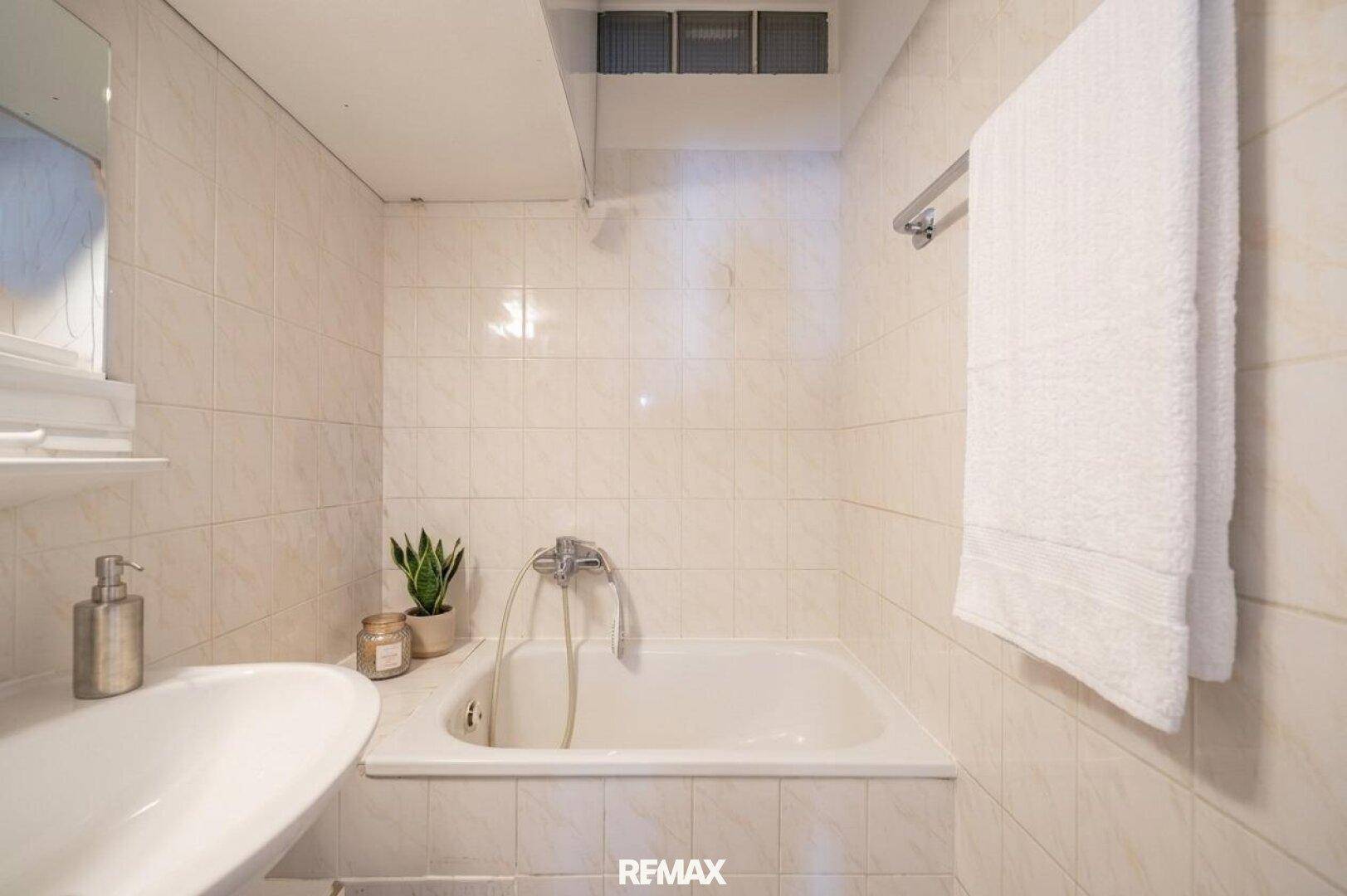 Gefliestes Badezimmer mit Badewanne und Waschbecken, in hellem, funktionalem Design.