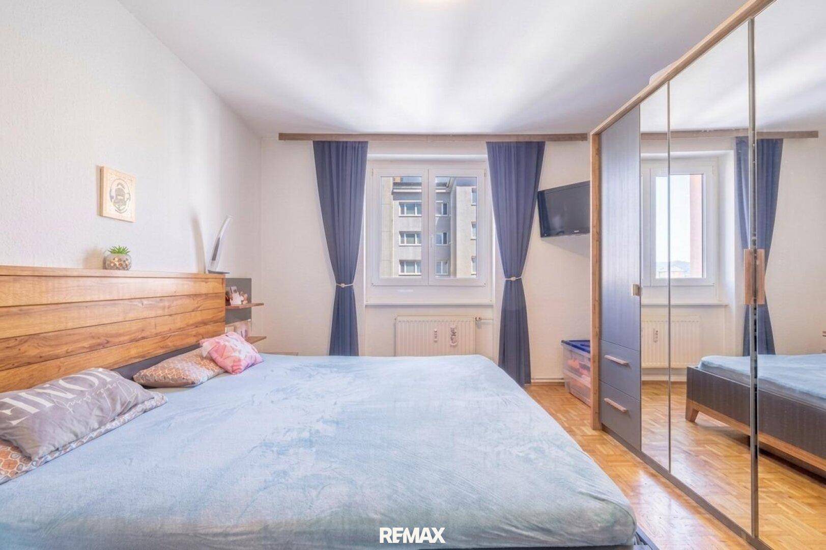 Geräumiges Schlafzimmer mit Doppelbett, großem Spiegelschrank und zwei Fenstern.