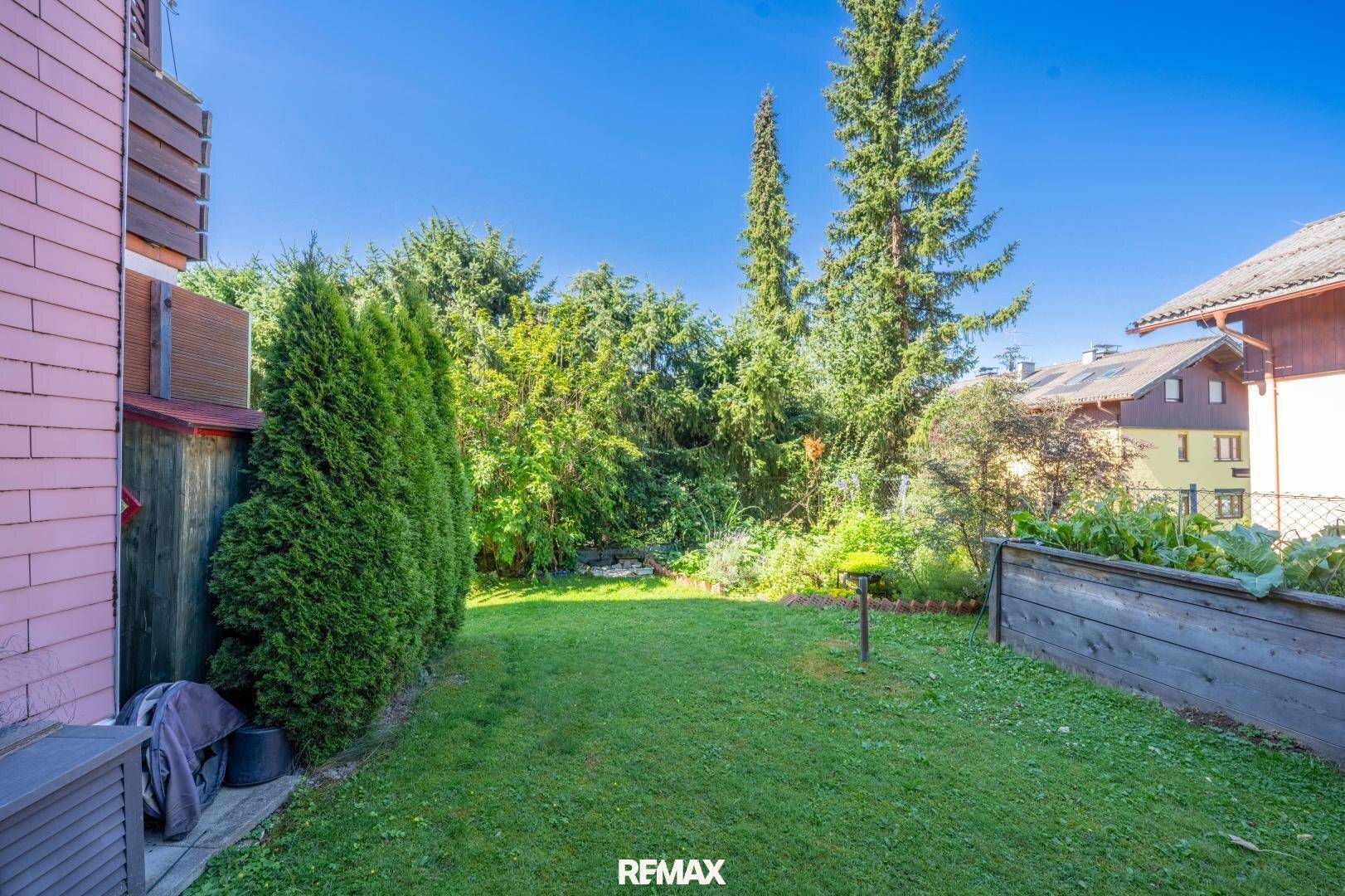 Gepflegter Gartenbereich mit Rasenfläche, Bäumen und einem Hochbeet, ideal für den Anbau von Gemüse.