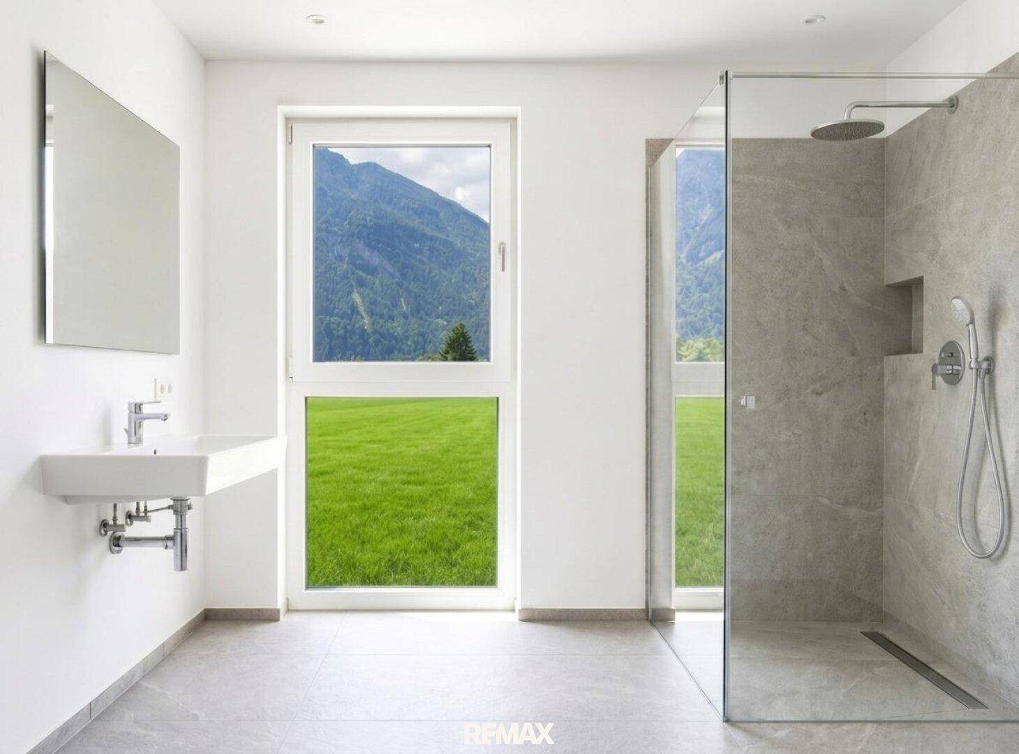 Modernes Badezimmer mit begehbarer Dusche, schwebendem Waschbecken und großem Fenster mit Bergblick.