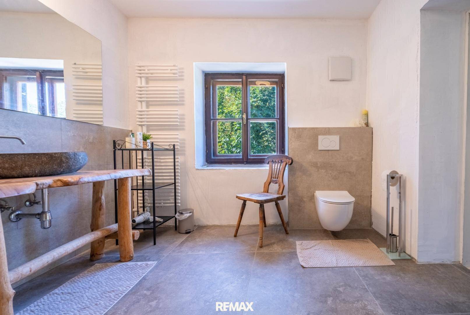 Rustikales Badezimmer mit Steinwaschbecken auf Holzkonsole, Fliesenboden und Fenster.