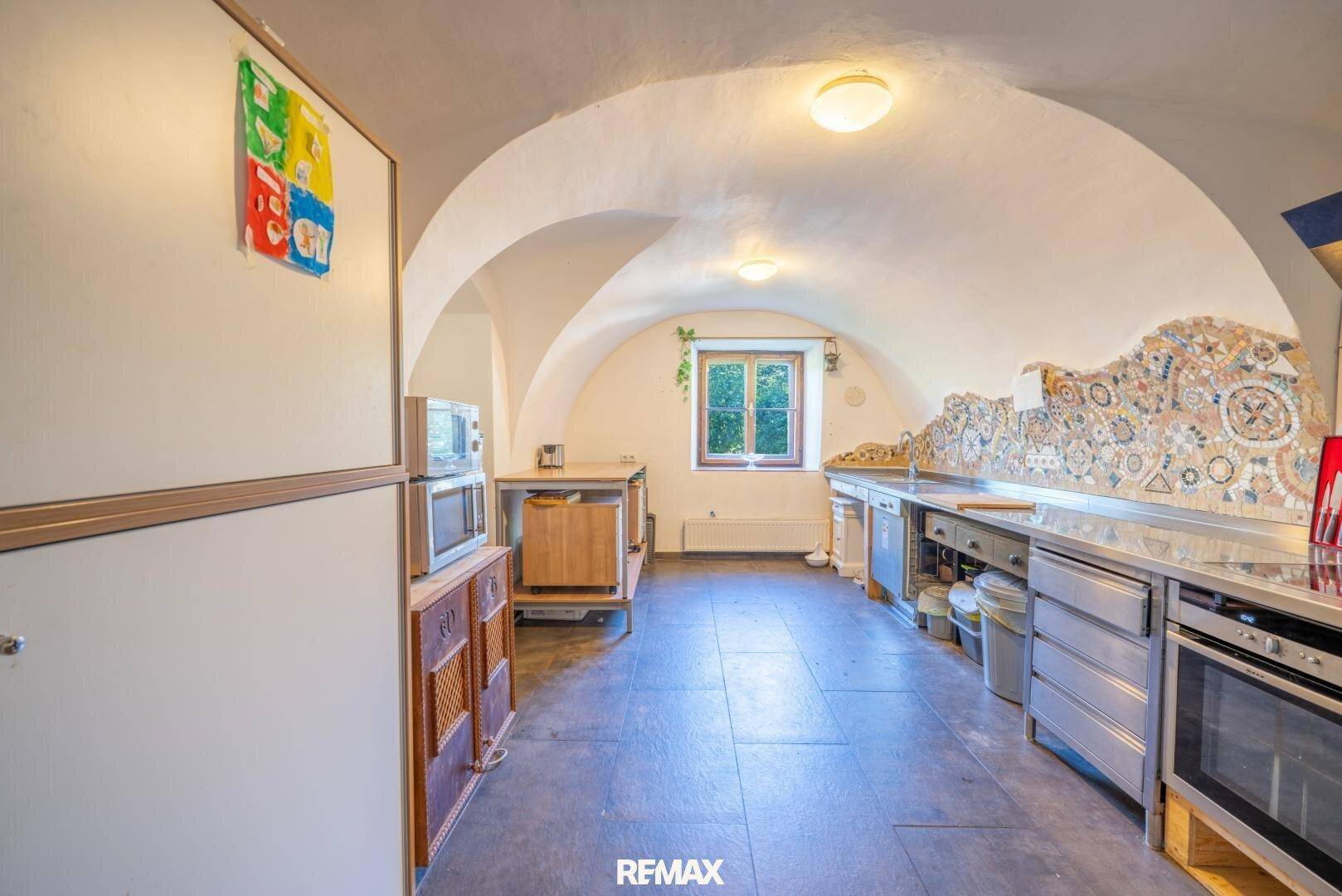 Rustikale Küche mit Gewölbedecke, Edelstahl-Arbeitsflächen und farbenfroher Mosaikwand.