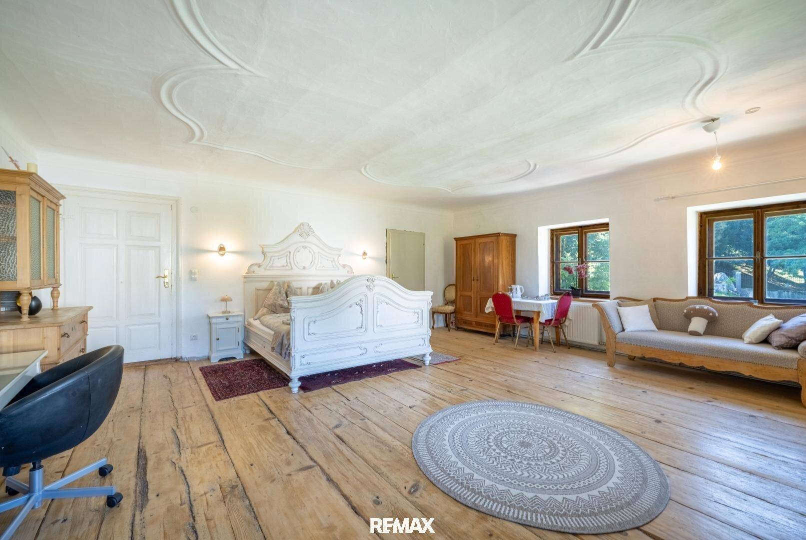 Geräumiges Schlafzimmer mit antikem Himmelbett, Holzdielenboden und dekorativer Stuckdecke.