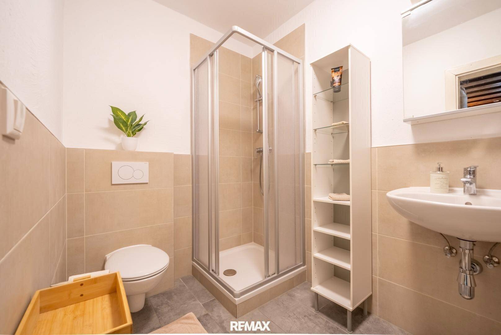 Kleines Badezimmer mit Duschkabine, WC und Waschbecken, hell gefliest.
