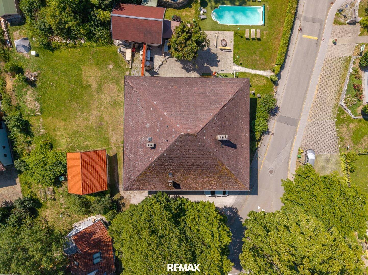 Vogelperspektive eines Hauses mit Satteldach, umgeben von Bäumen und einem Garten mit Pool.