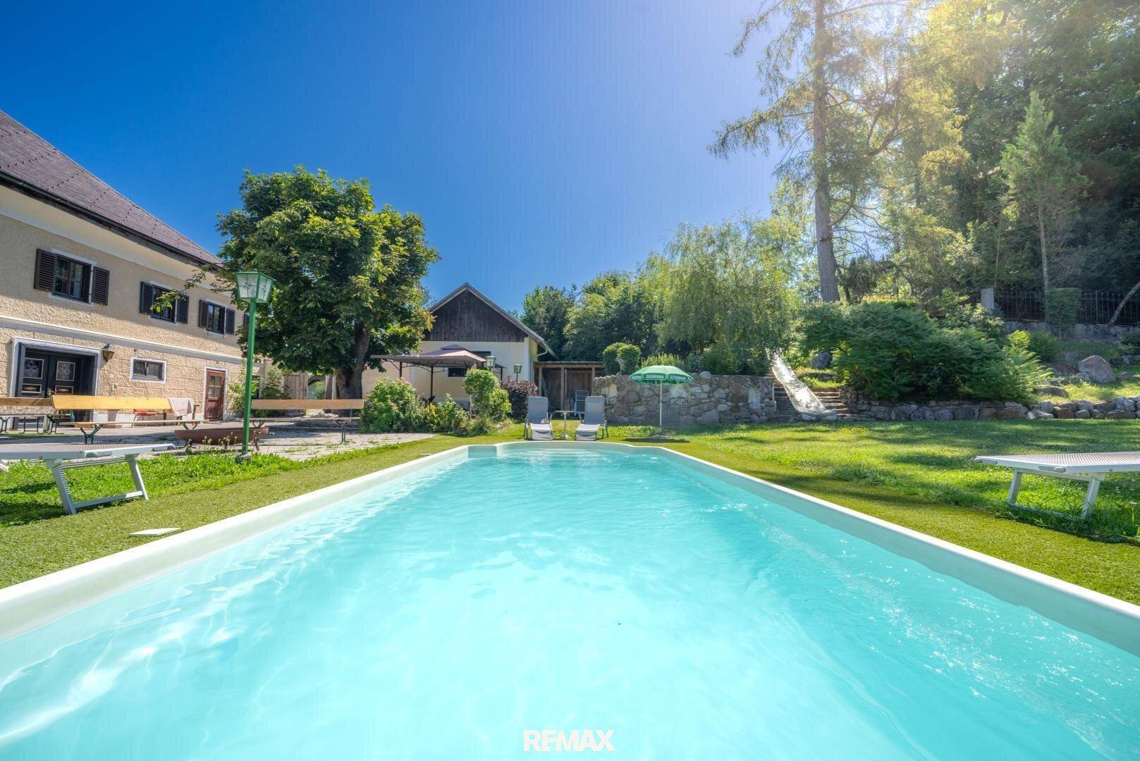 Großer Poolbereich im Garten mit Liegewiese und Blick auf das historische Gebäude.