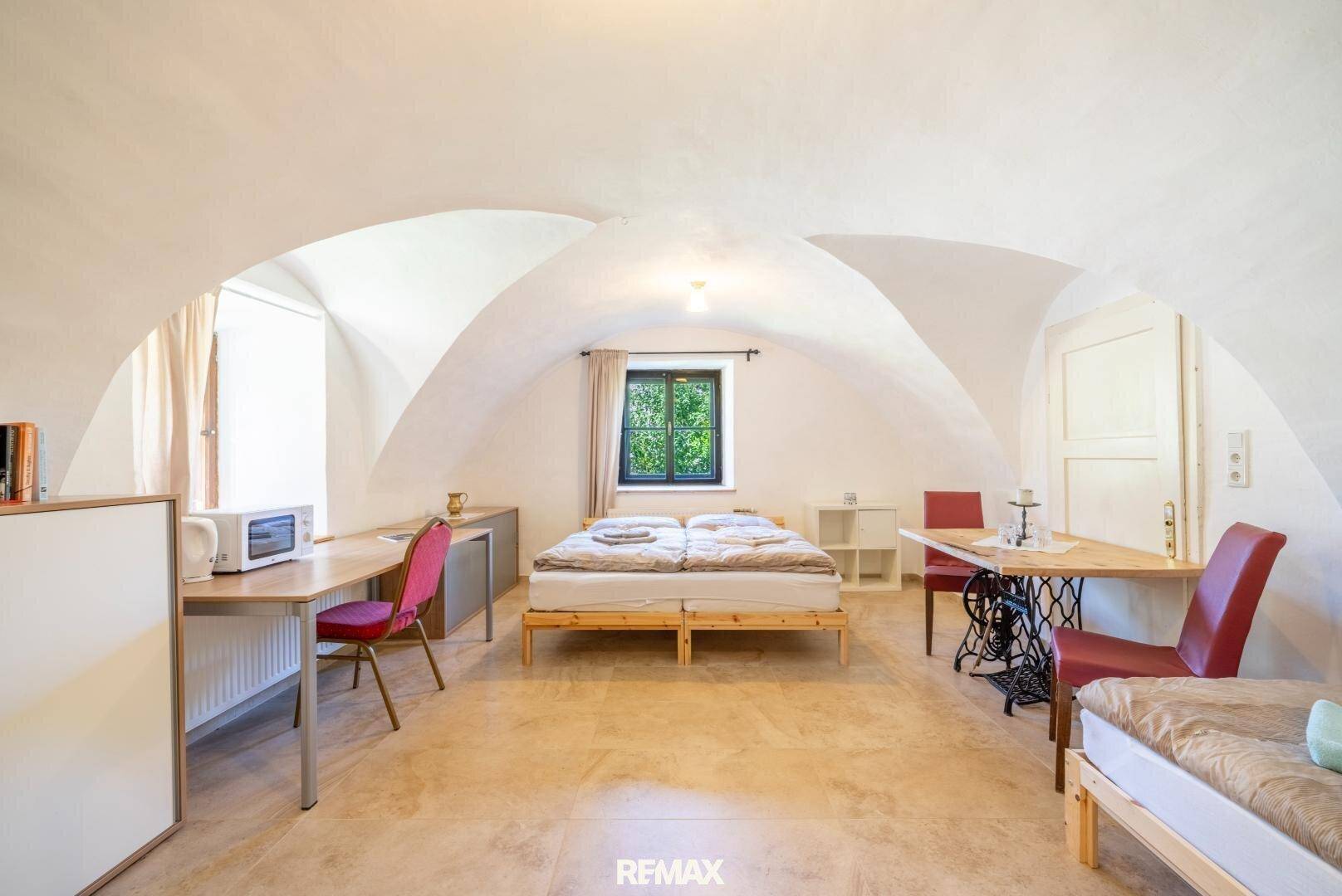 Schlafzimmer mit Gewölbedecke, Fliesenboden und Arbeitsbereich, hell und funktional eingerichtet.