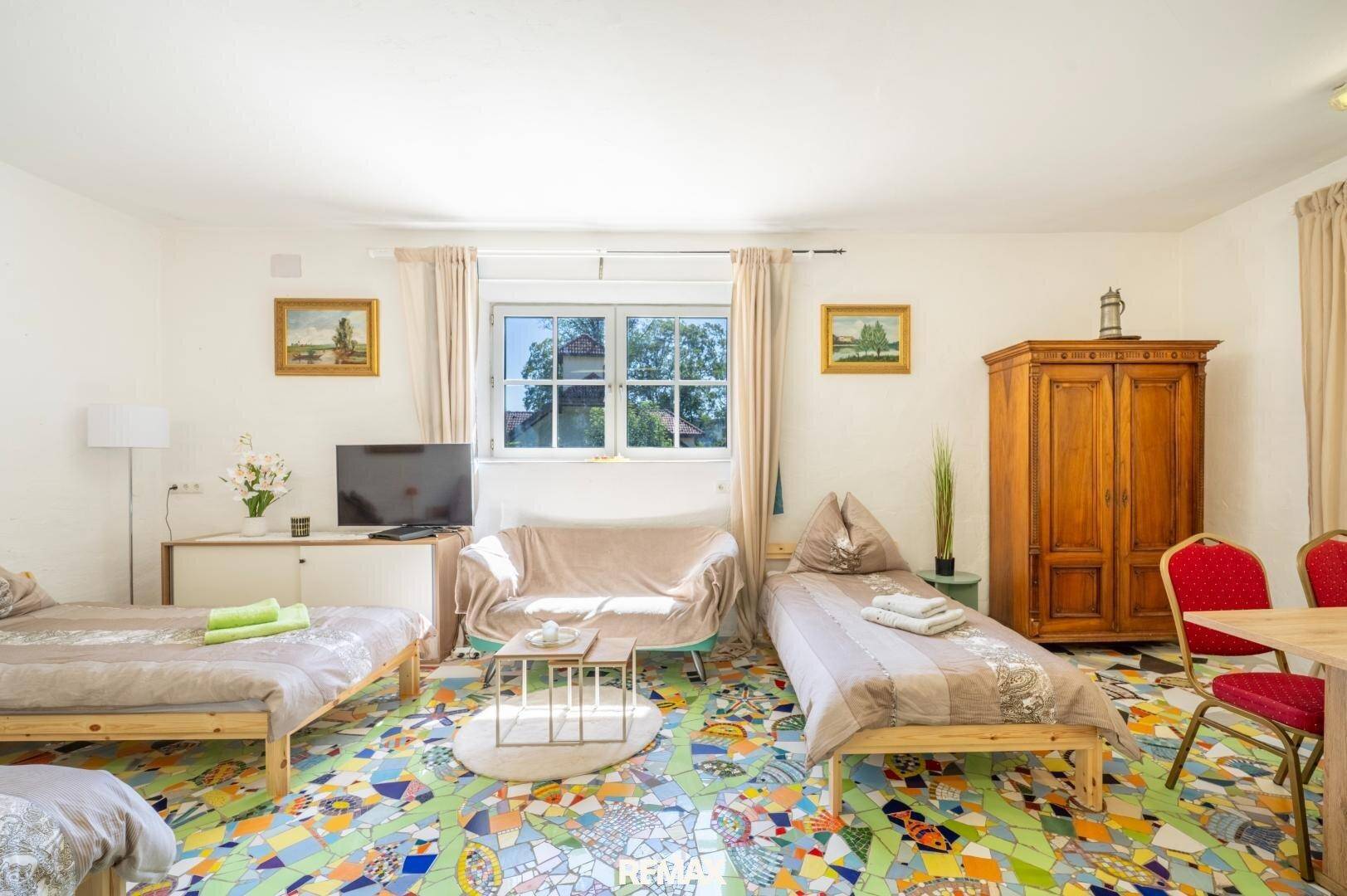 Helles Schlafzimmer mit farbenfrohem Mosaikboden, Einzelbetten und Blick ins Grüne.