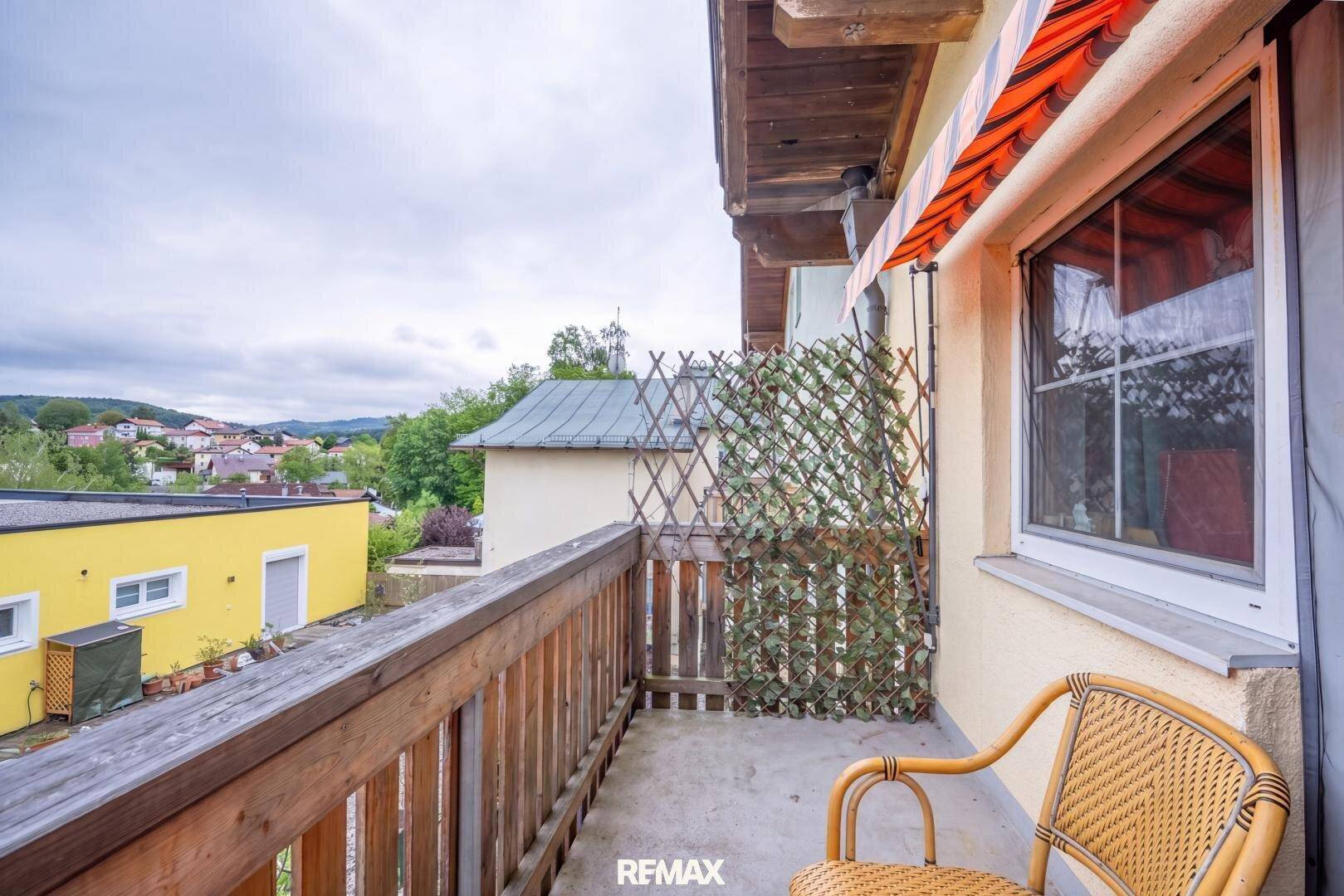 Kleiner Balkon mit Holzgeländer, Korbstuhl und Blick auf die Umgebung.