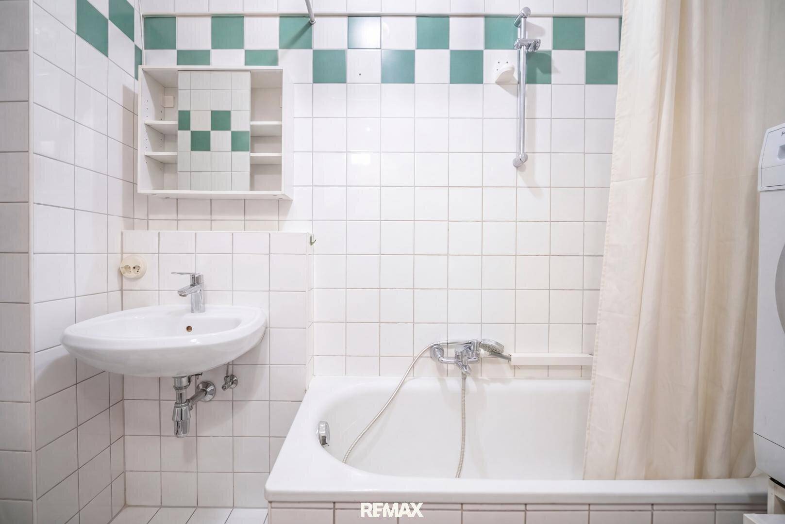 Badezimmer mit Badewanne, Waschbecken und grün-weiß gefliesten Wänden.