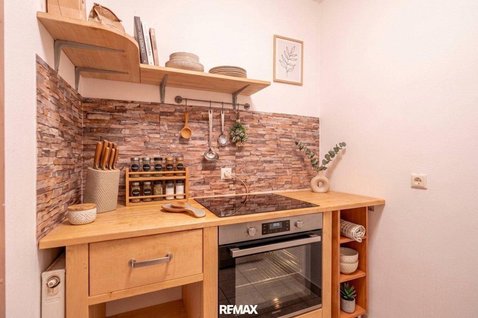 Kompakte Küchenzeile mit Holz-Arbeitsplatte, Steinoptik-Rückwand und integriertem Backofen.