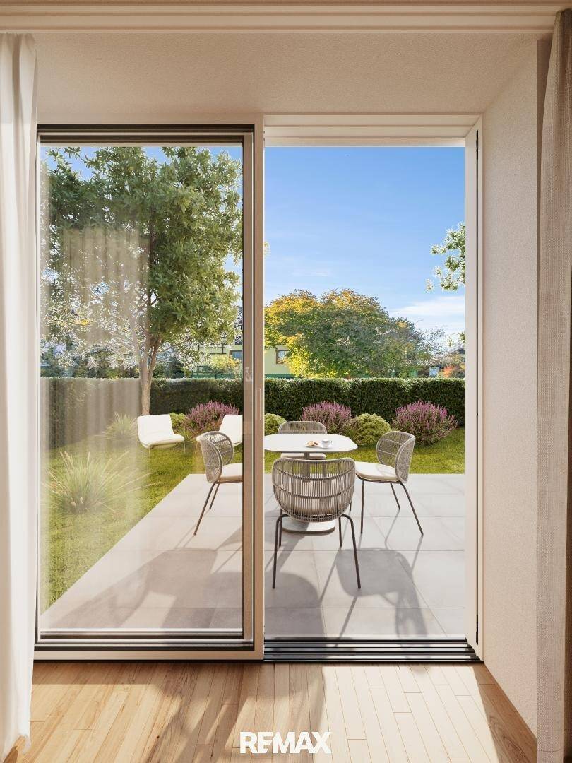 Blick aus dem Wohnbereich auf die Terrasse mit Gartenmöbeln und grüner Umgebung.